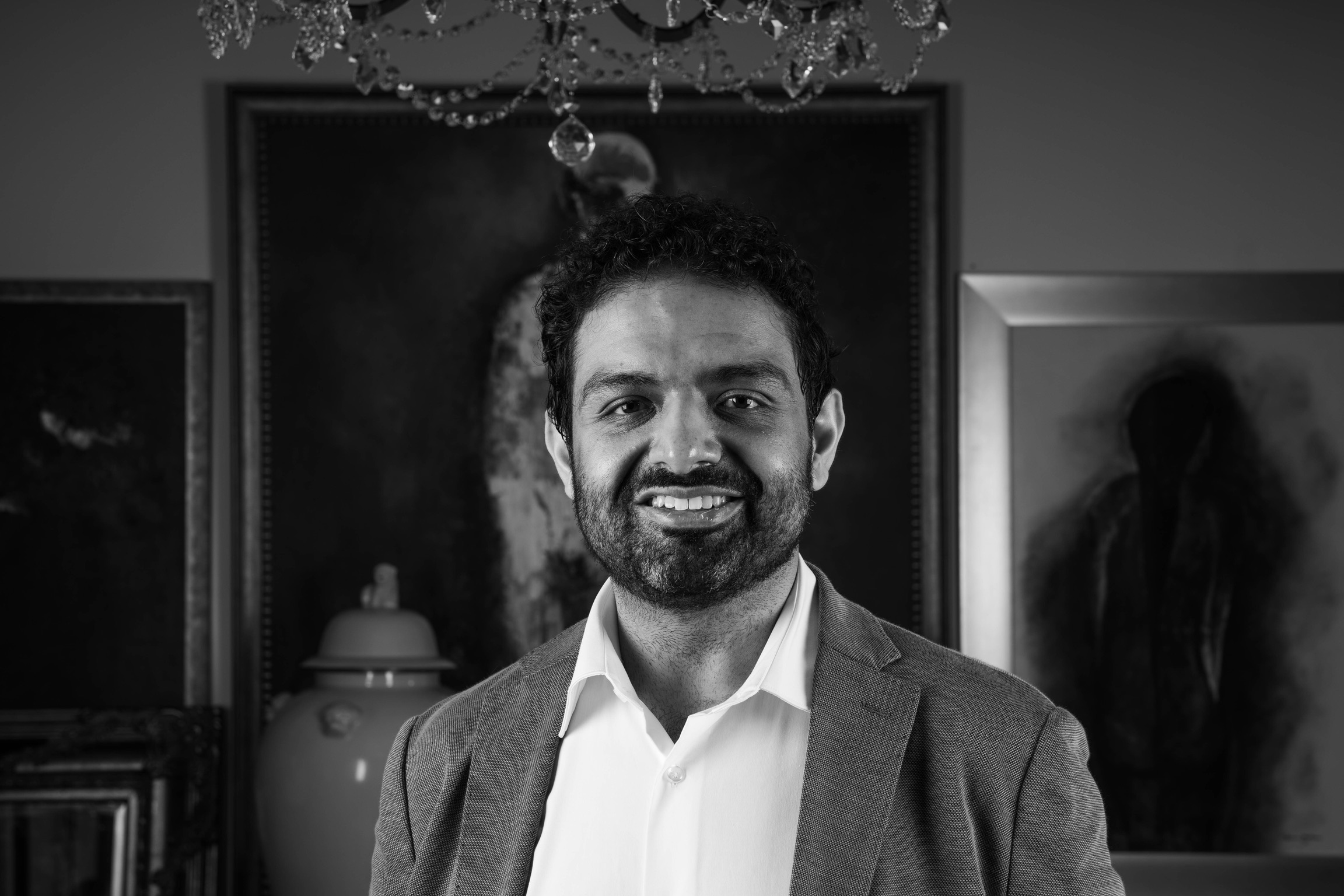 Tariq Ismail, black and white portrait beneath a chandelier with artworks behind