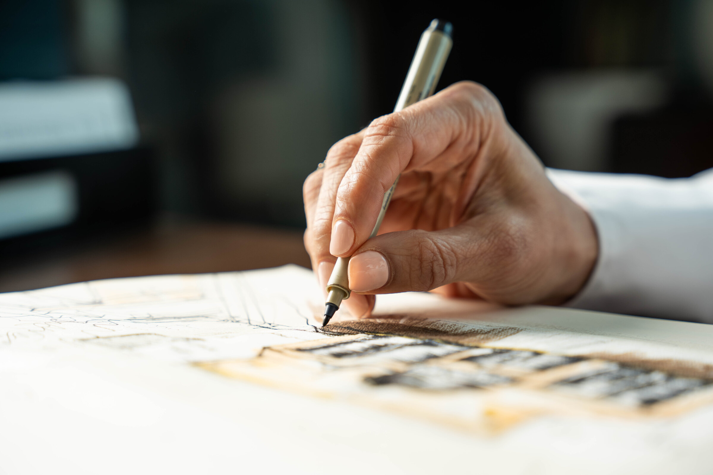 A hand working in the studio sketchbook, ink and wash over an architectural elevation
